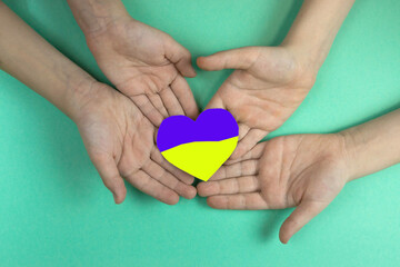 Children's hands hold a paper-cut heart painted in the colors of the Ukrainian flag. People of Ukraine. Children's hands flag Ukraine .Selective focus