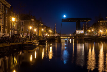 Leiden, The Netherlands, March 18, 2022, night view of the canal with historic houses and small boats and full moon