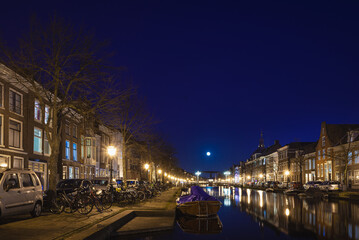 Fototapeta na wymiar Leiden, The Netherlands, March 18, 2022, night view of the canal with historic houses and small boats and full moon
