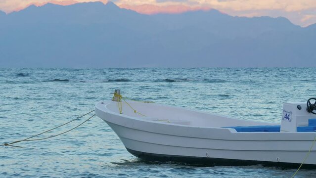 Empty white motorboat is rocking on Red sea waves. Fishing boat swaying on ripple water surface in windy day. Motor ship, outboard runabout floating near seaside. Travel, tourism, fishery