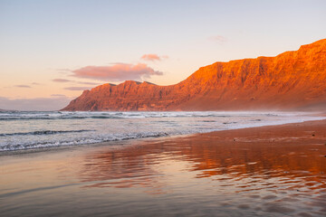 Obraz premium View of amazing beach during red sunset time. Ocean water and shore. Mountains in background with clear sky. Summer holiday vacationand scenic beautiful destination.
