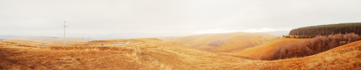 Caucasian autumn countryside with fields in a mountain valley and dense forest on the right side. Panoramic view