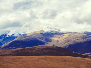 Autumn field at the foot of the Caucasian mountains covered with snow under the clouds. A sharp temperature drop in the highlands. An unusual occurrence.