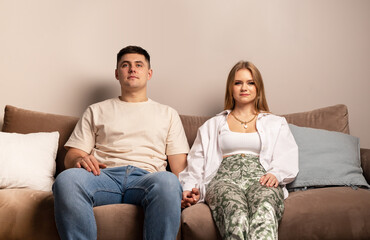 Young couple sitting on couch, watching TV and holding hands. Calm weekend spending, happy family...