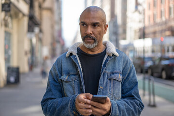 Mature black man in city using cell phone walking on a street