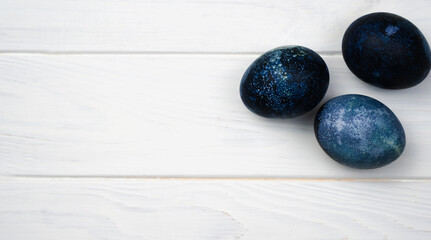 Easter eggs painted with natural dye in blue on the white wooden background. Banner. Close-up. Top view. Place for text.