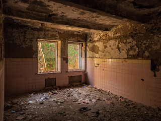 A shabby ruined room of an old abandoned building with remnants of tiles, piles of rubbish on the...
