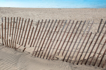 Broken snow fence in beach sand with blue lake water - Powered by Adobe