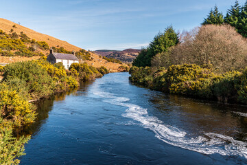 Fototapeta na wymiar River passing near an old Irish cottage in a beautiful spring scenery. Mountain rustic landscape.