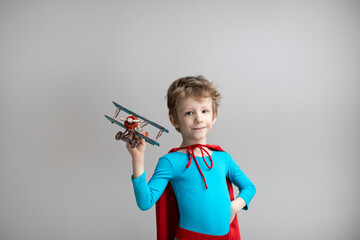 Little superhero boy in a red cape plays with an airplane. Happy smiling child. Success, motivation and travel.