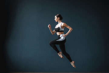 Beautiful fitness woman in a jump full length over gray