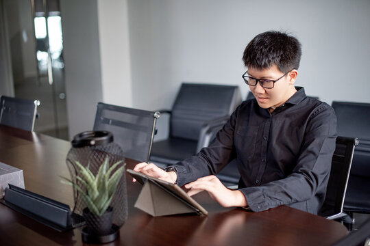 Young Asian businessman using digital tablet in office meeting room. Male entrepreneur reading news on social media app. Online marketing and Big data technology for E-commerce business. 