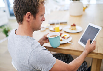 Enjoying breakfast time. Shot of a handsome man using his tablet while having breakfast at home.