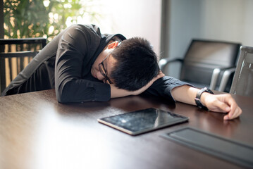 Overworked Asian businessman sleeping in office meeting room with digital tablet on conference table. Exhaustion and health problems from overload working concept