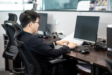 Asian businessman wearing glasses dressed in black working with computer in office. Work routine urban lifestyle. Business and technology concept