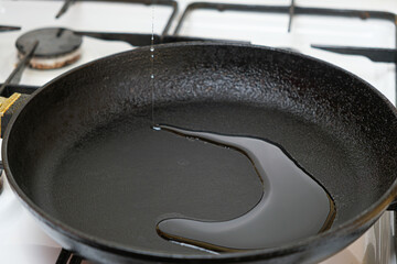 The process of pouring vegetable oil into a cast iron heated frying pan.