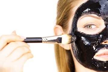 Woman applying black mud mask to face