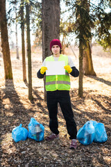 Male nature activist holds white template paper while standing near blue trash bags