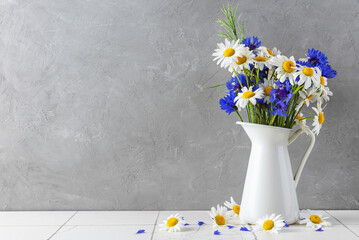 beautiful wildflowers bouquet made of white chamomile flowers and cornflowers in vase on gray...