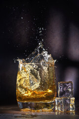 Glass of old whiskey with ice. A splashing glass of whiskey with ice isolated on a dark background