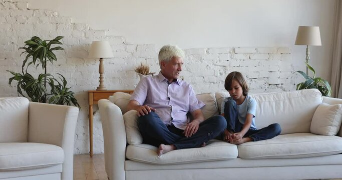 Loving multi generational family, older granddad his pre-teen grandson talking seated on couch at home, little grandkid share news, lead pleasant reliable conversation with grandfather, trust concept