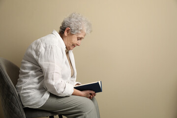 Elderly woman with poor posture reading book on beige background. Space for text