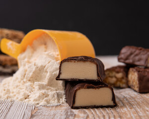 a sweet bar made of whey protein next to a scoop of protein powder for sports nutrition.