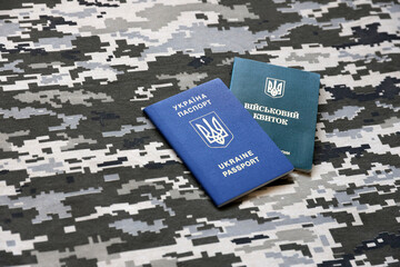 Ukrainian military ID and foreign passport on fabric with texture of pixeled camouflage. Cloth with...