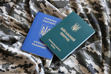 Ukrainian military ID and foreign passport on fabric with texture of pixeled camouflage. Cloth with...