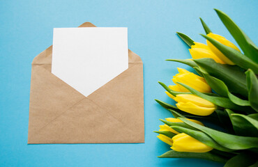 Envelope with white paper for text on blue background and yellow tulips. A spring holiday greetings