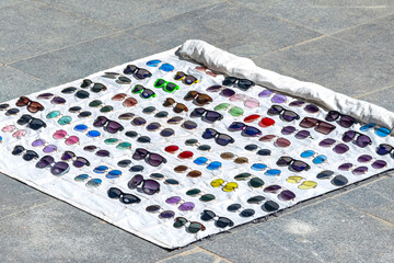 Collection of imitation sunglasses displayed on a blanket on the ground to offer to tourists
