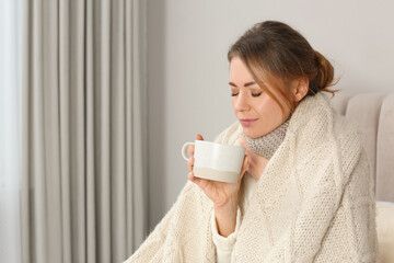 Sick woman with warm plaid and cup of drink in bed at home