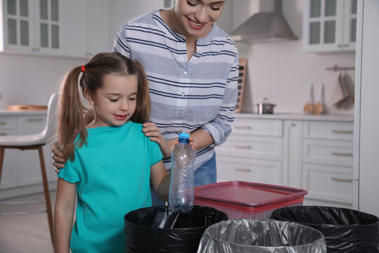 Young woman and her daughter throwing plastic bottle into trash bin in kitchen. Separate waste collection