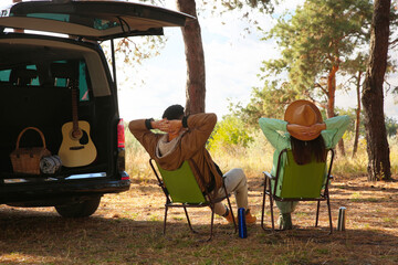 Couple with thermoses resting in camping chairs on autumn day, back view