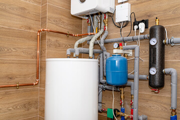Water tank and gas pipes for a modern gas boiler in a home boiler room, lined with ceramic tiles.