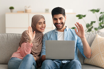 Muslim Couple Making Video Call Via Laptop Waving Hands Indoor