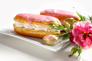 Glazed buns with cream on a plate, a cup of tea and a flower on a white background. Photo