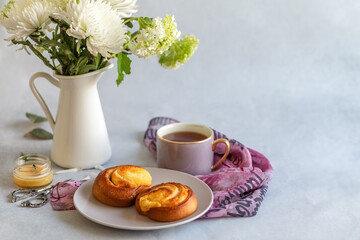 Sweet buns on a plate. Flowers in a vase and a cup of tea. Photo