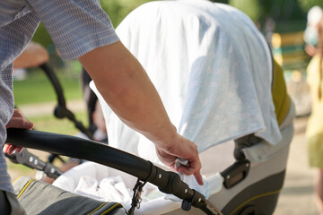 Close-up of men's hands with a stroller. A young father, straightens the cape on the stroller. Father's Day Concept. High quality photo