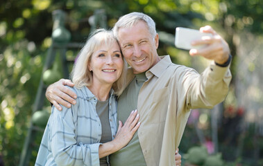 Happy elderly couple spending time in their garden together, taking selfies and smiling at cellphone camera