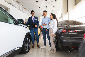Young couple buying new auto at car showroom - obrazy, fototapety, plakaty