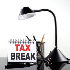 TAX BREAK text on notebook with pen and table lamp on the black background