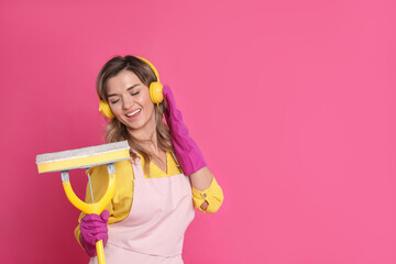Beautiful young woman with headphones and mop singing on pink background. Space for text