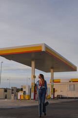 chica guapa con pelo largo y rizado y camisa de colores andando frente a una gasolinera