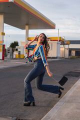 chica guapa con pelo largo y rizado y camisa de colores andando frente a una gasolinera