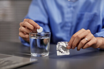 Close up of unrecognizable businesswoman putting fizzing pill into glass of water at workplace, copy space