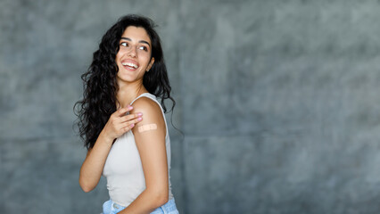 Coronavirus vaccination. Happy young woman showing band aid on her arm, looking aside at free space...