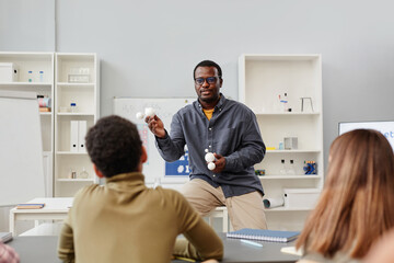 Front view portrait of African American science teacher explaining chemistry to group of children...