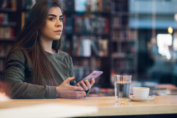 Woman using smartphone and drinking coffee in a cafe.