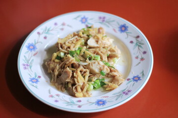 Ginger-fried chicken with sliced spring onions served on a white floral plate on an orange dining table.